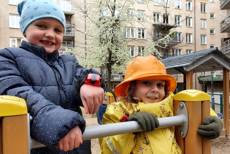Två förskolebarn visar accelerometrarna de har på handlederna
